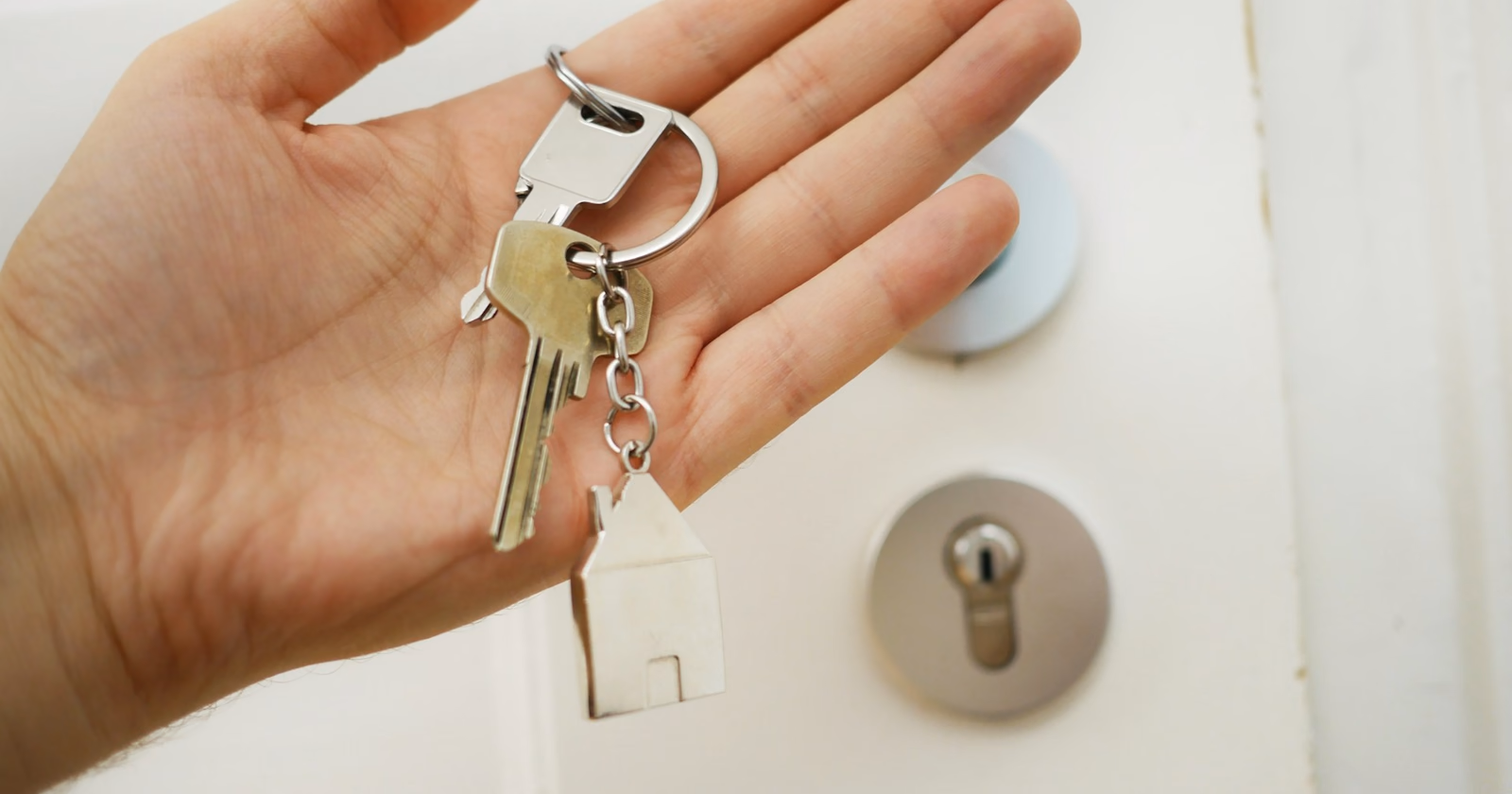 Una mano sostiene unas llaves con un llavero de casa ante la cerradura de una puerta
